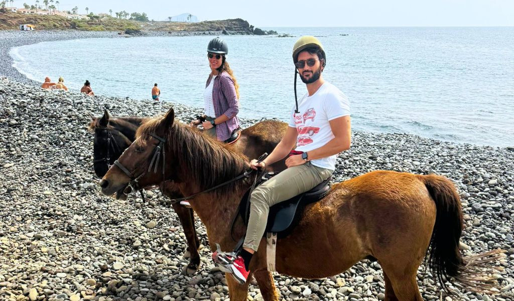 Des gens à cheval sur la plage de galets de Tenerife, avec la mer en arrière-plan.