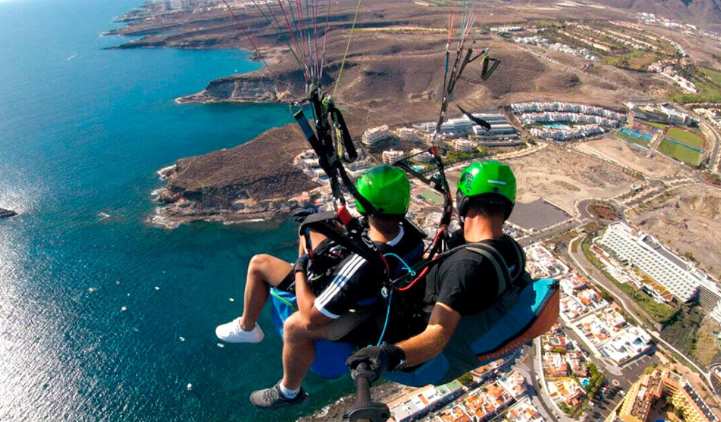 Des gens parapentant au-dessus de la côte de Tenerife avec vue aérienne sur la mer et les bâtiments.