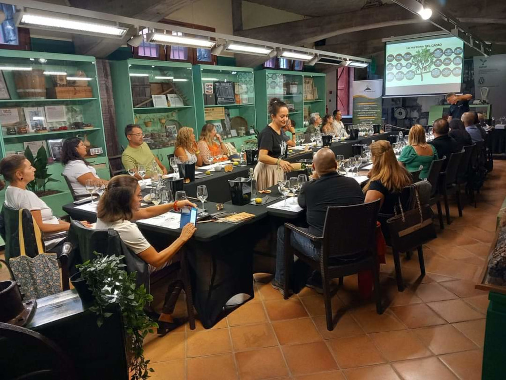 Des gens à une dégustation de vin dans une salle décorée à Tenerife. Texte visible : L’anatomie du cacao.