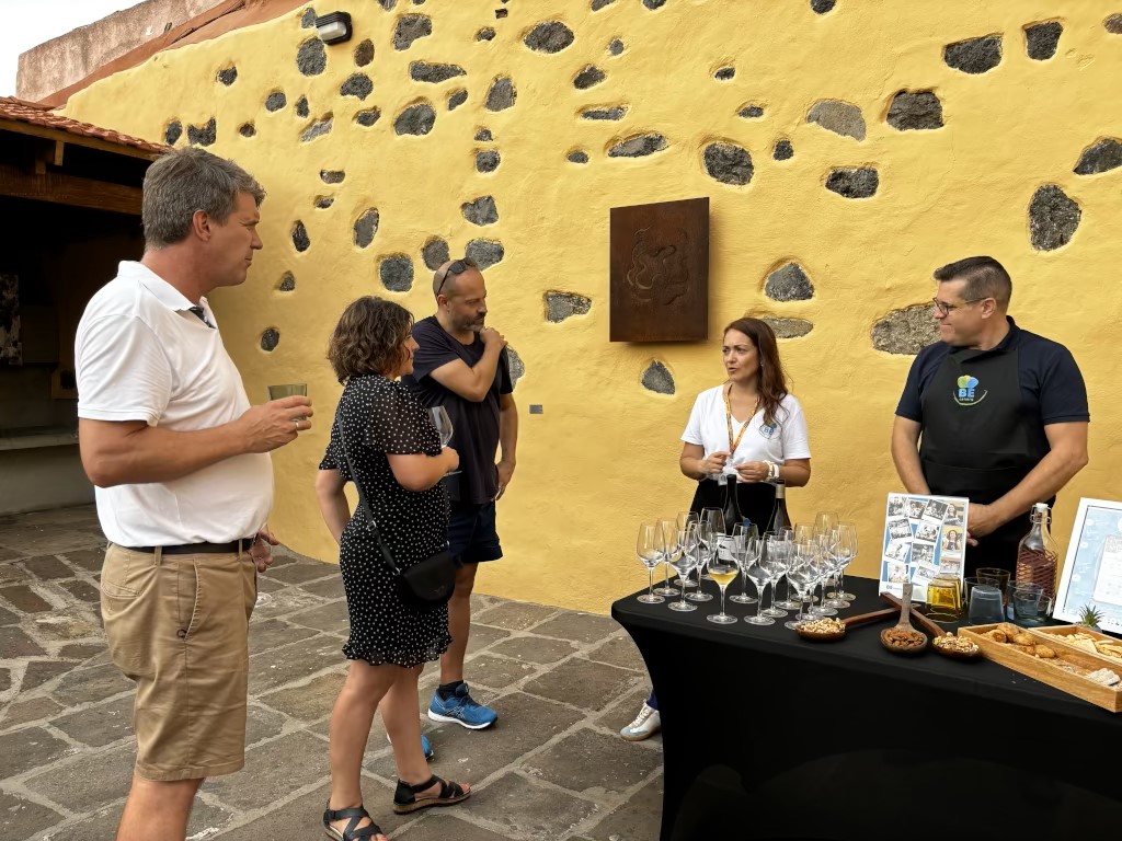 Groupe de personnes à dégustation de vin à Tenerife, à côté d’une table avec boissons et encas.
