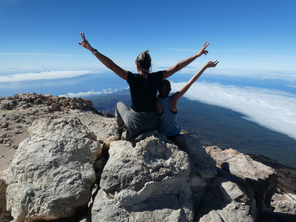 Des gens lèvent les bras au sommet du mont Teide à Tenerife, surplombant le paysage nuageux.