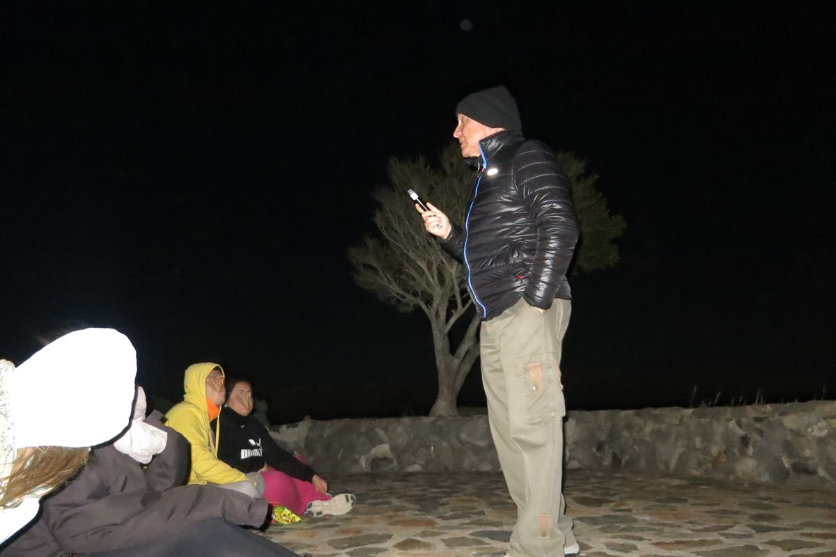 Personne qui parle dehors la nuit à Tenerife, avec un groupe assis à proximité.
