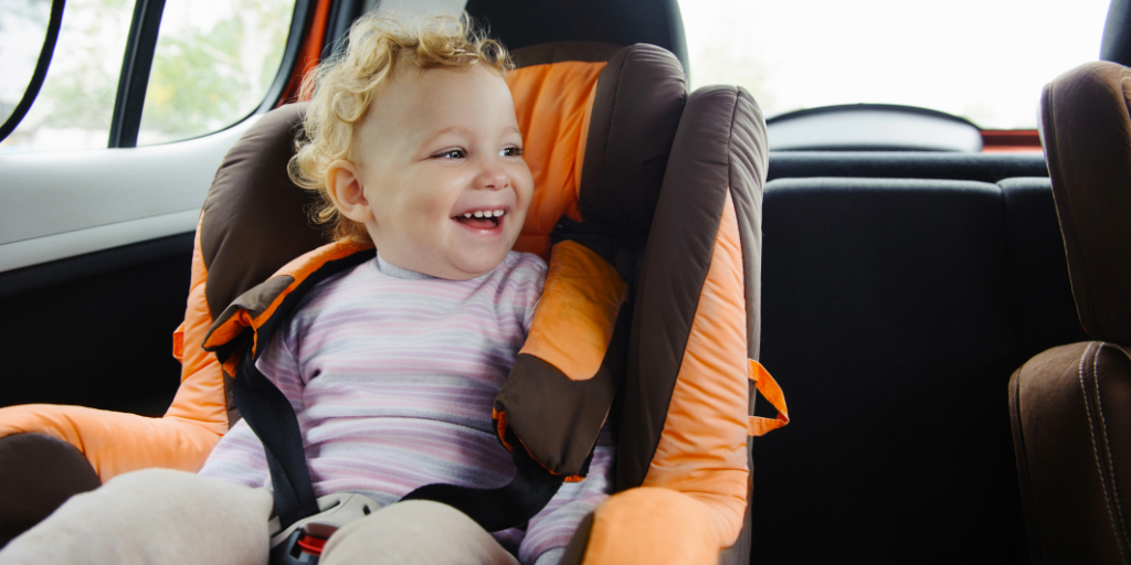 Enfant souriant dans un siège auto à l’intérieur d’une voiture.