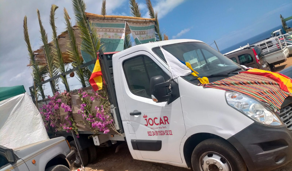 Camion décoré de fleurs et de drapeaux à Tenerife, avec une vue partielle sur la mer.