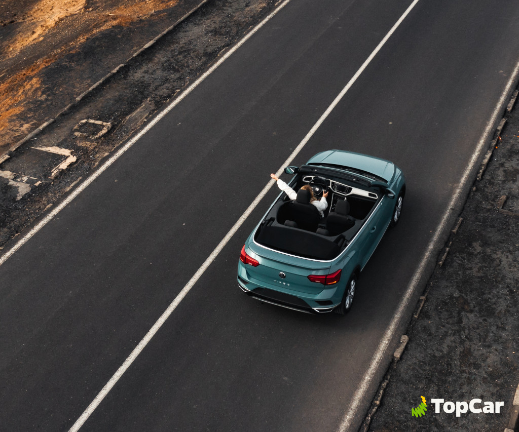 Une personne conduisant une décapotable bleue sur la route à Tenerife. Texte visible : TopCar.