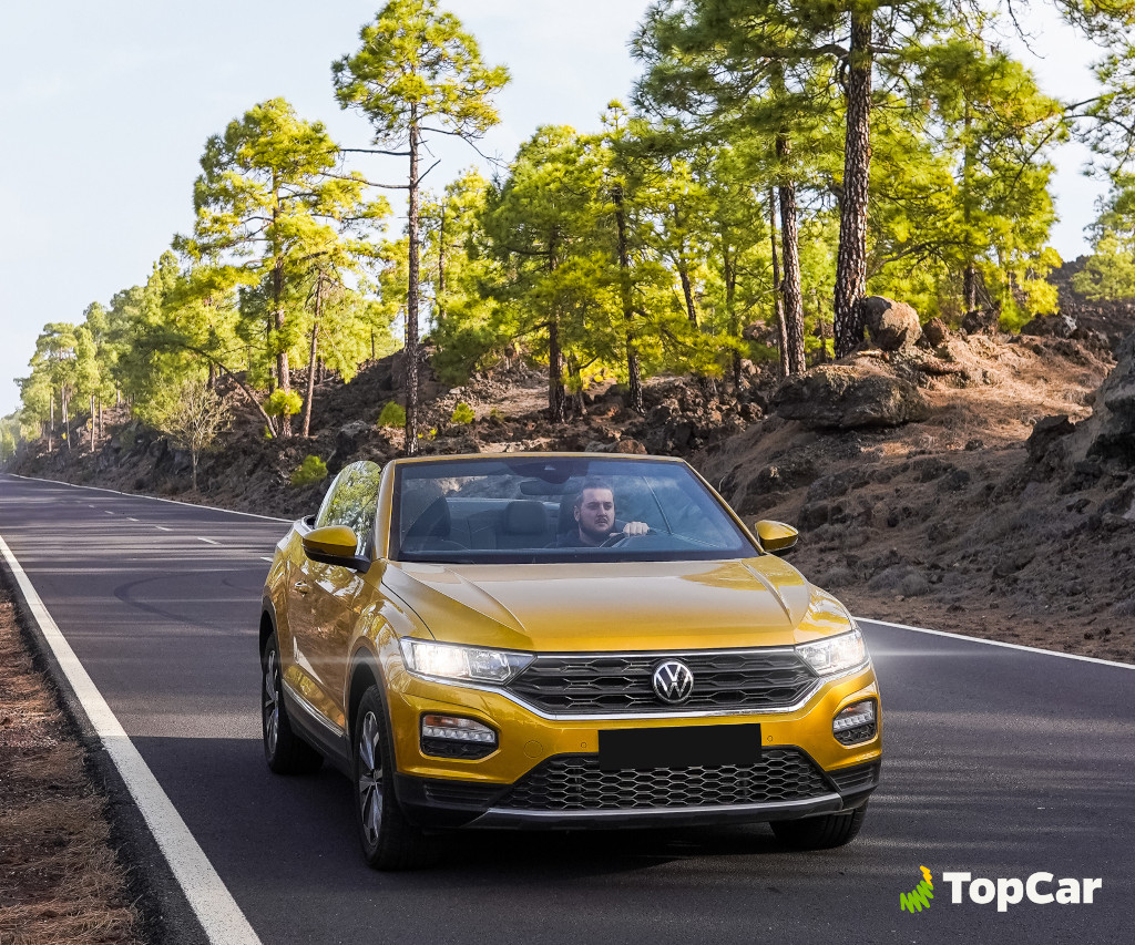 Voiture jaune sur la route entourée de pins à Tenerife. Logo TopCar.