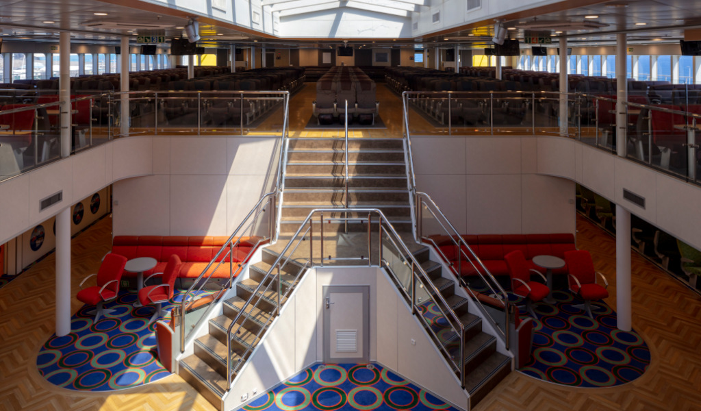 Salon intérieur d’un ferry à Tenerife avec chaises et tables rouges.
