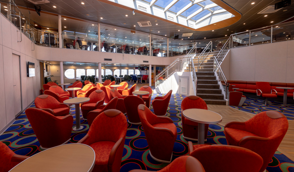 Salon intérieur d’un ferry près de Tenerife avec chaises rouges et escaliers.