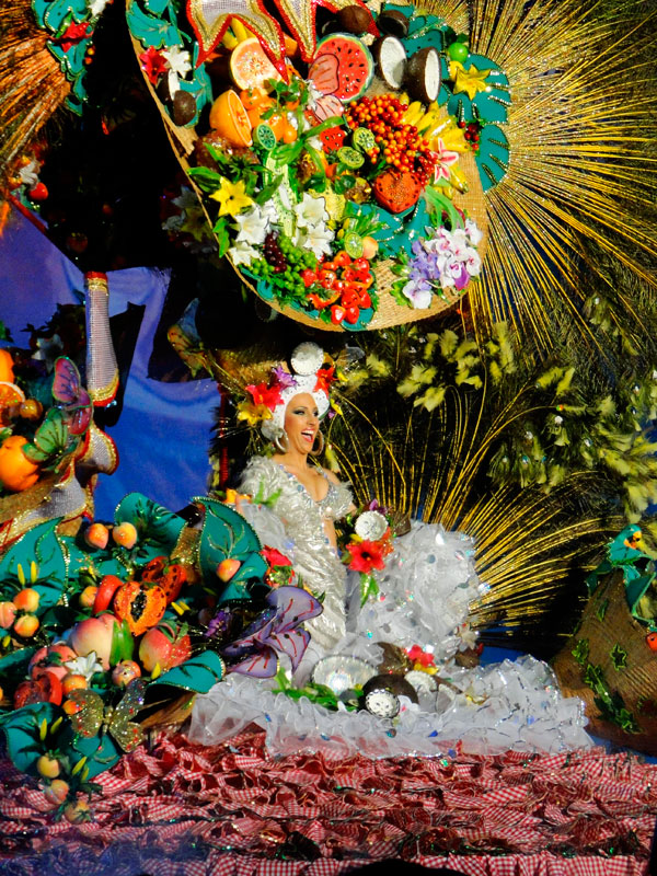 Personne souriante en costume coloré de fruits et de fleurs, participant au carnaval de Tenerife.