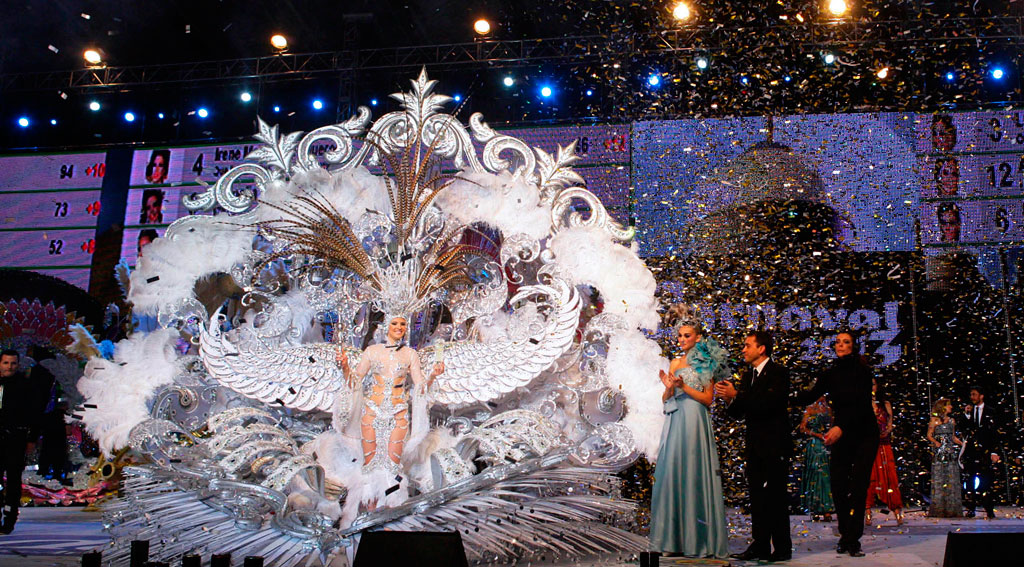 Personne en costume orné au Carnaval de Tenerife, entourée de confettis et de lumières.