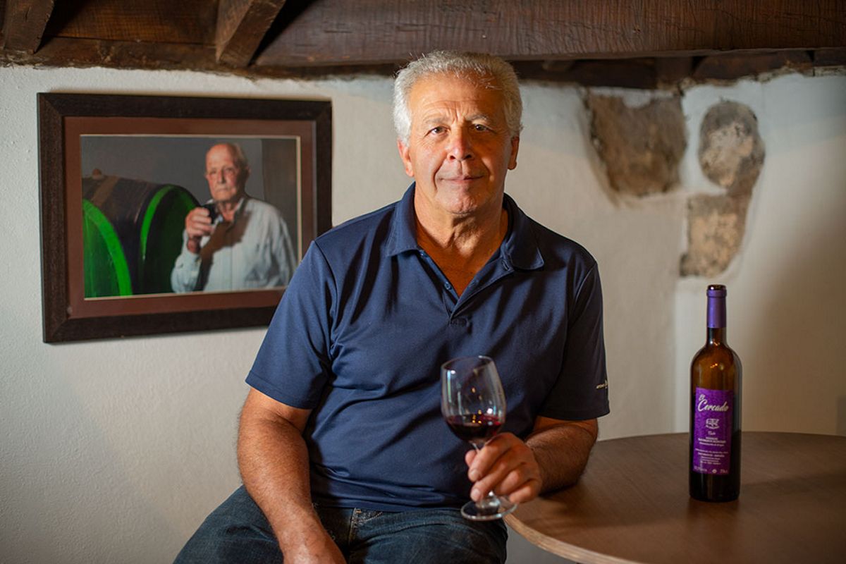 Un homme tenant un verre de vin à côté d’une bouteille et d’un portrait dans la cantina de Tenerife.