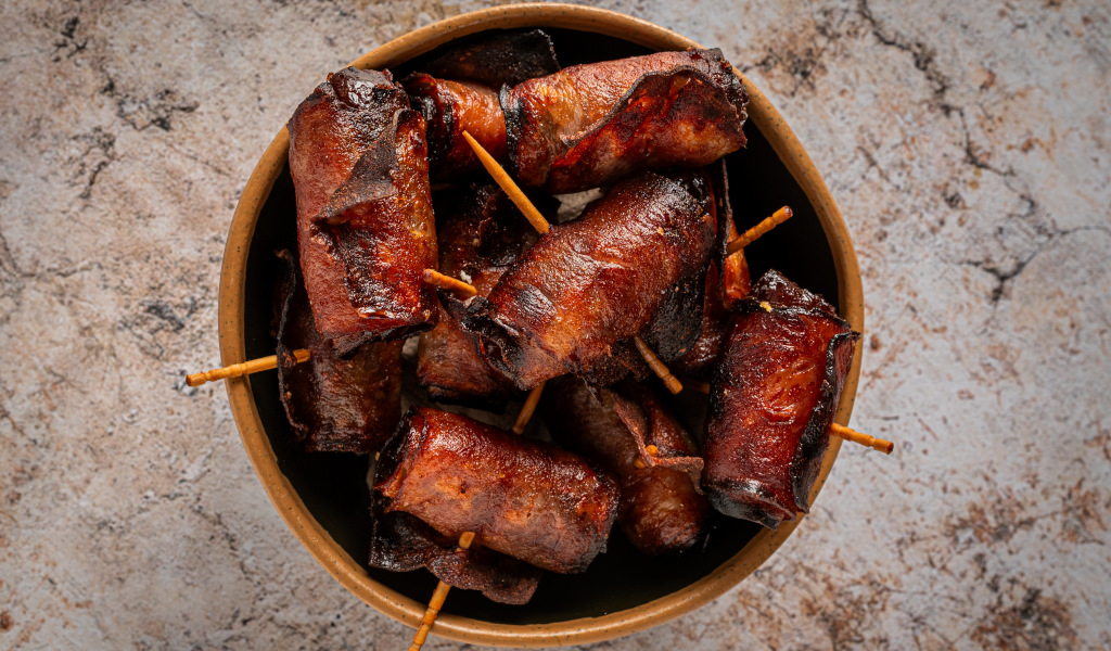 Des saucisses enveloppées de bacon avec des baguettes sur fond en pierre.