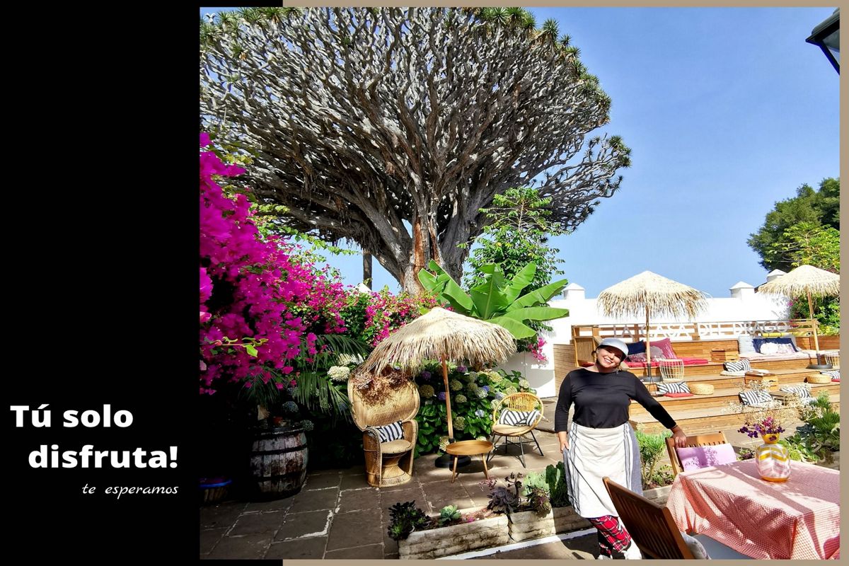 Terrasse avec végétation, parasols en paille et une personne à Tenerife. Texte : Profitez-vous simplement ! Nous vous attendons.