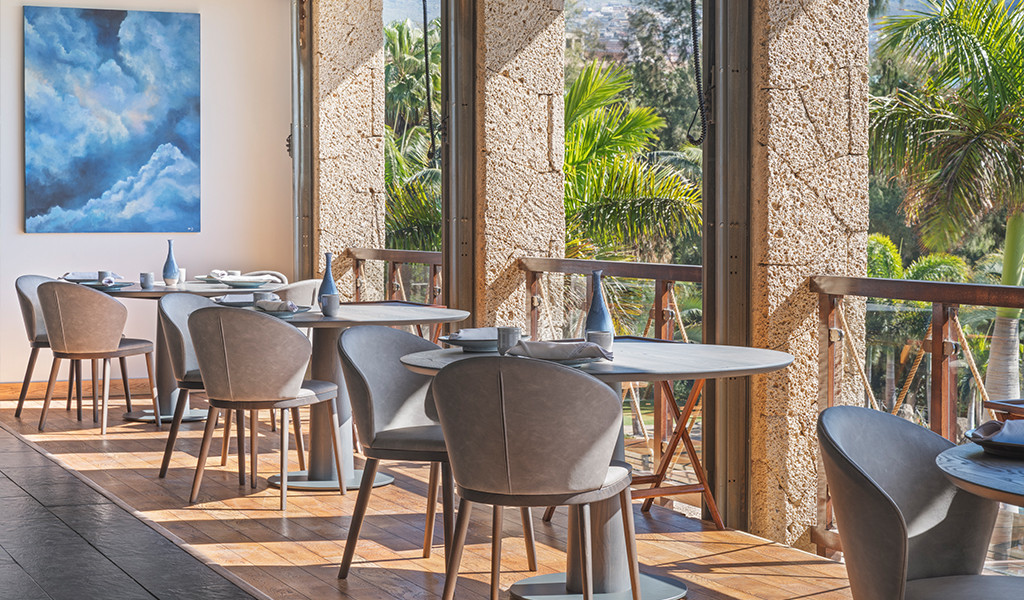 Salle à manger avec tables et chaises à côté de grandes fenêtres donnant sur les jardins de Tenerife.