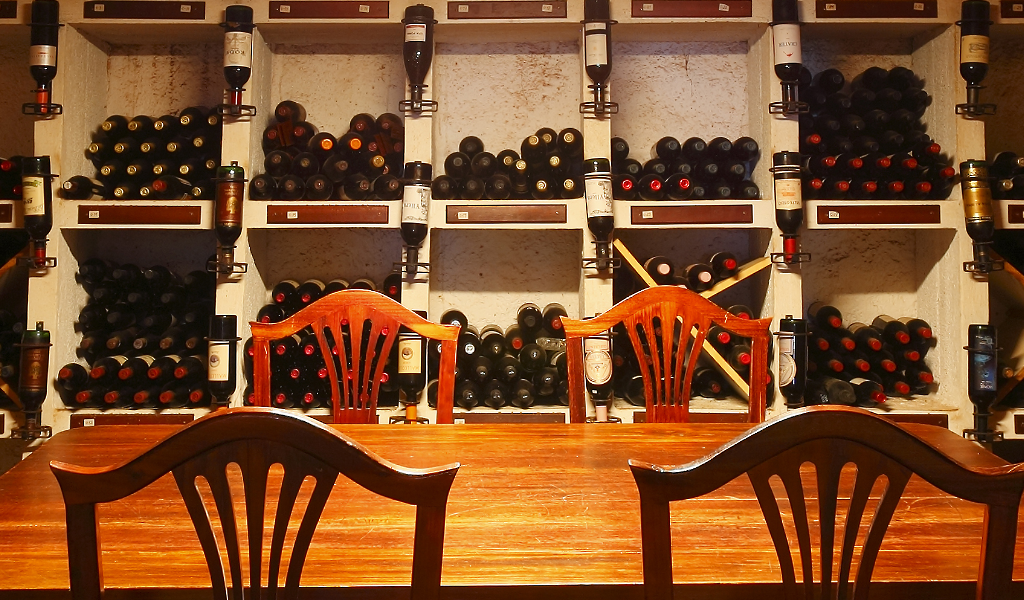 Table en bois et chaises devant une étagère pleine de bouteilles de vin à Tenerife.