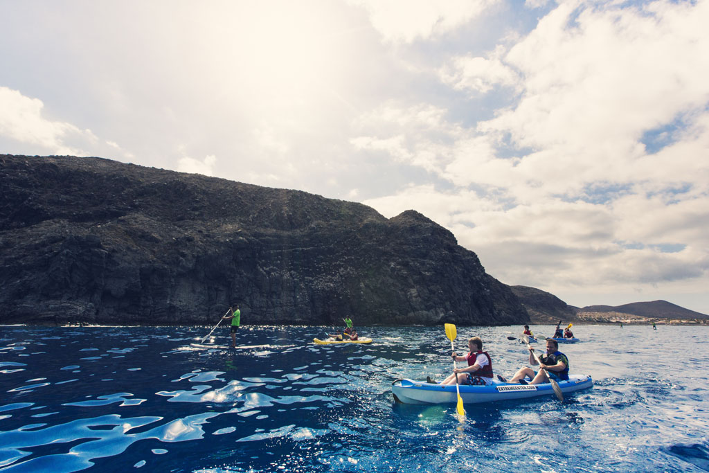 Des gens font du kayak et du paddle surf sur la côte de Tenerife, avec des montagnes en arrière-plan.