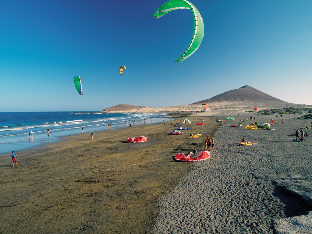 Des gens qui font du kitesurf sur la plage d’El Médano, à Tenerife, avec des montagnes en arrière-plan.