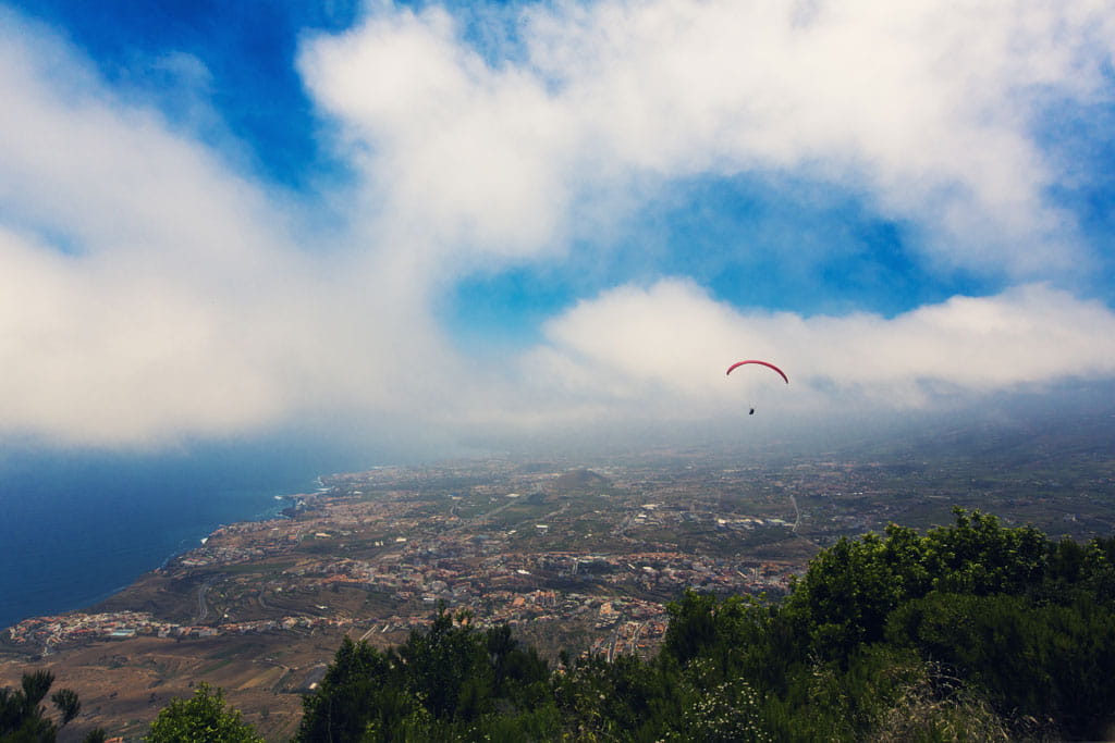 Parapente survolant le paysage côtier de Tenerife sous un ciel partiellement nuageux.