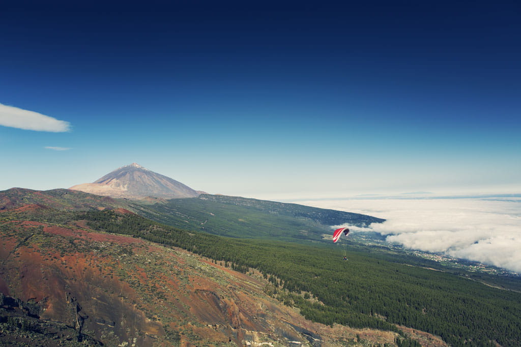 Parapente au-dessus du mont Teide à Tenerife, avec des nuages et un paysage volcanique.