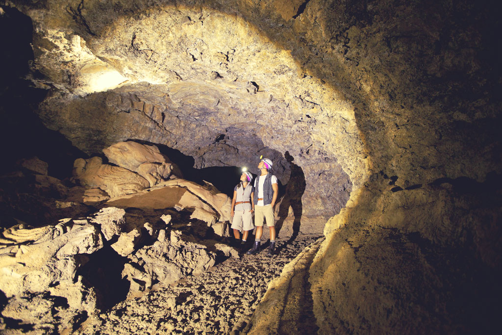 Des gens explorant une grotte volcanique à Tenerife avec des casques et des lampes torches.