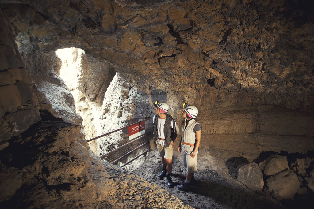 Deux personnes portant un casque explorent une grotte à Tenerife, sous la lumière naturelle qui pénètre.