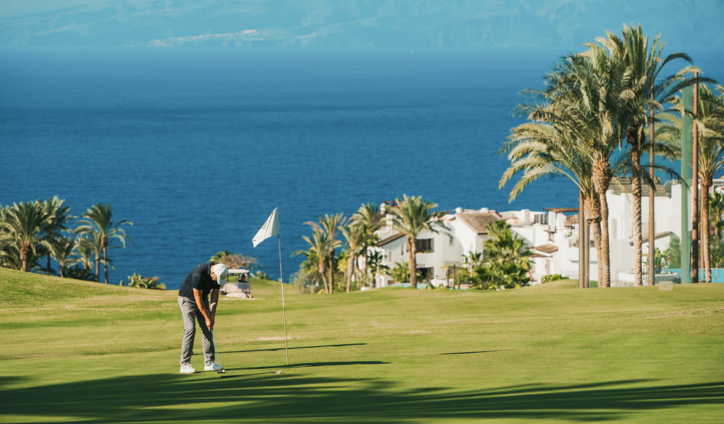 Personne jouant au golf sur un parcours avec vue sur la mer et des maisons à Tenerife.