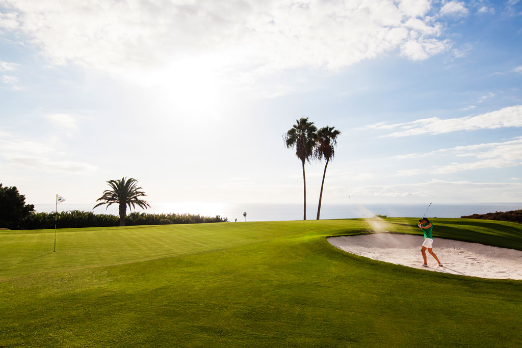 Personne jouant au golf sur un parcours en bord de mer à Tenerife avec des palmiers et un ciel dégagé.