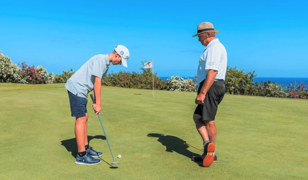 Enfant jouant au golf avec un adulte en arrière-plan, Tenerife.