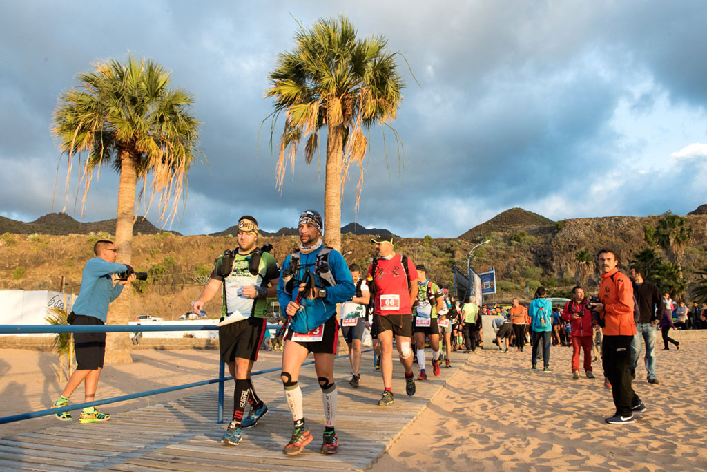 Les coureurs marchent le long de la plage de San Andrés, à Tenerife, avec des palmiers en arrière-plan.