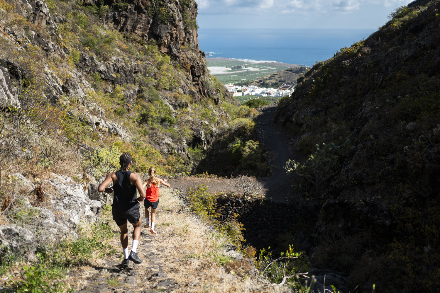 Des gens courant le long d’un sentier montagneux à Tenerife, surplombant la mer et la vallée.