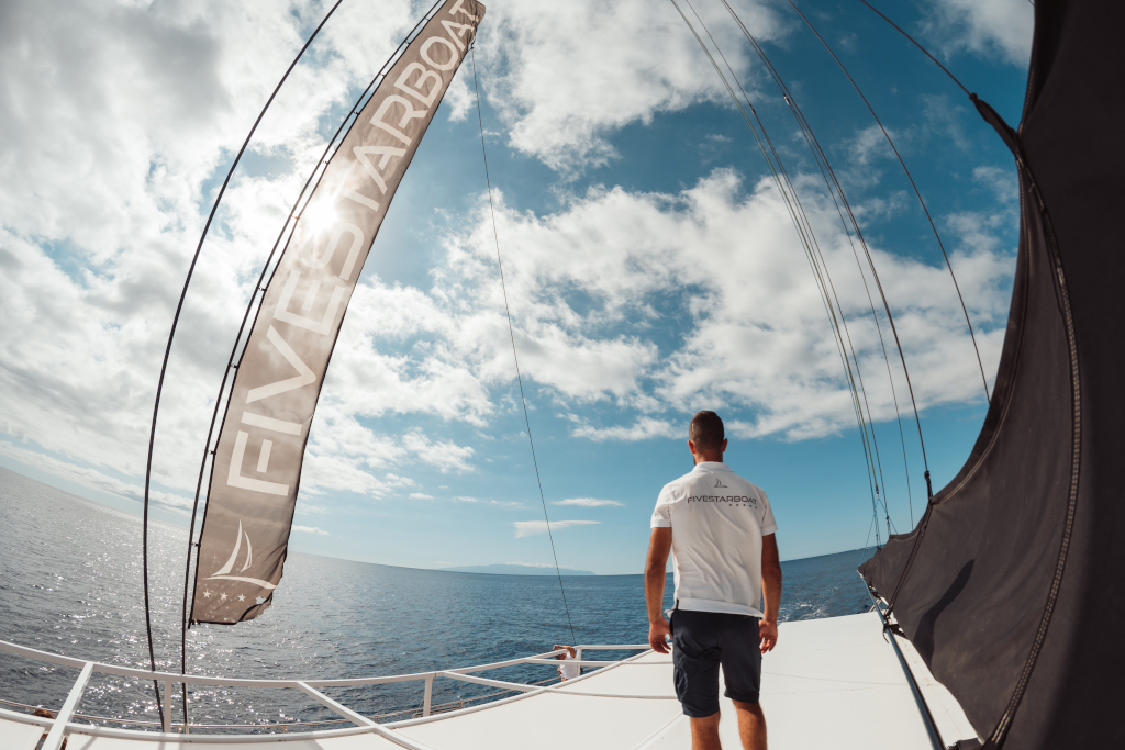 Personne à la proue d’un bateau portant un T-shirt sur lequel est écrit FIVESTARBOAT, regardant la mer à Tenerife.