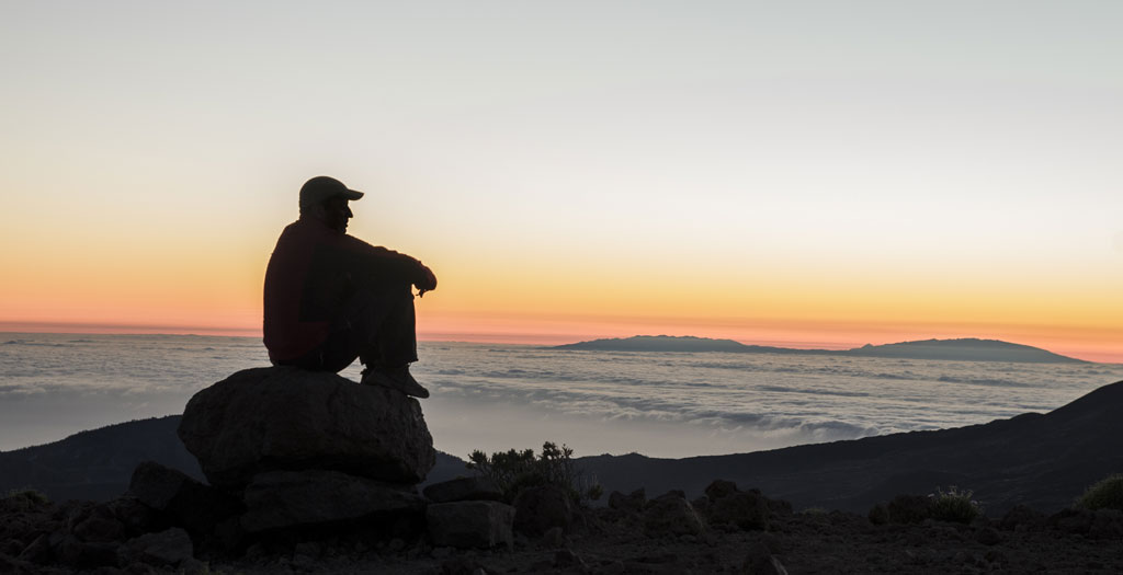 Personne assise sur un rocher regardant le coucher de soleil à Tenerife.