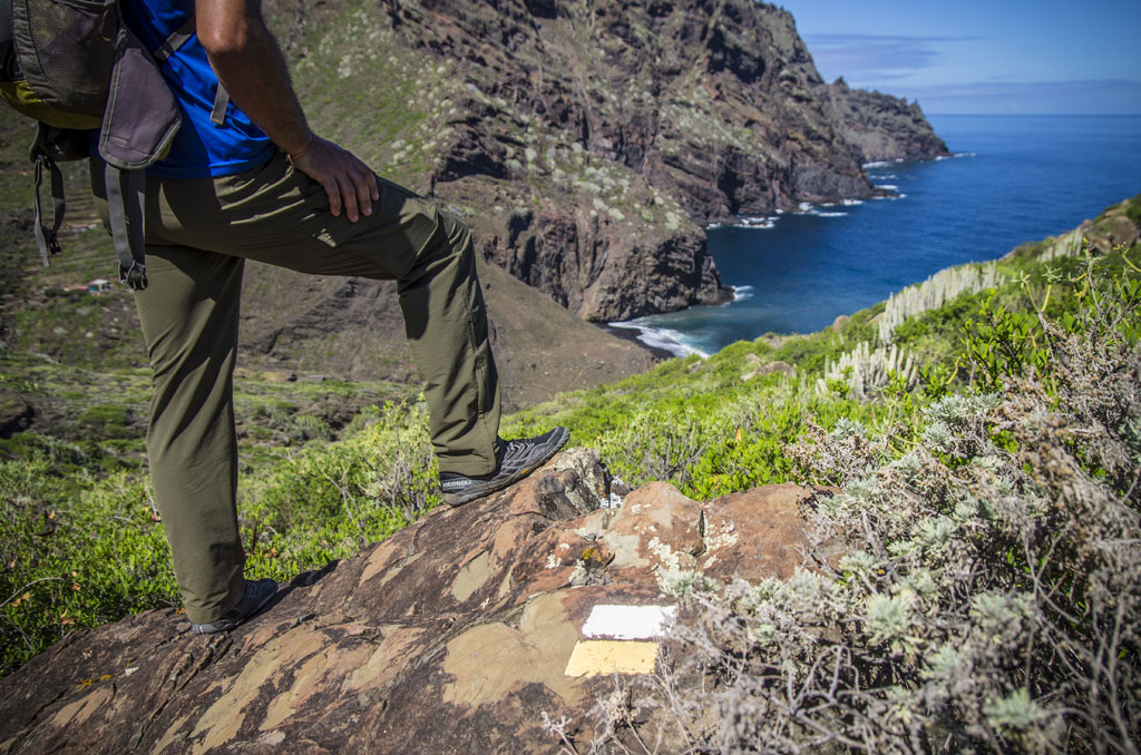 Personne avec un sac à dos posé sur un rocher sur un sentier à Tenerife avec vue sur la mer.