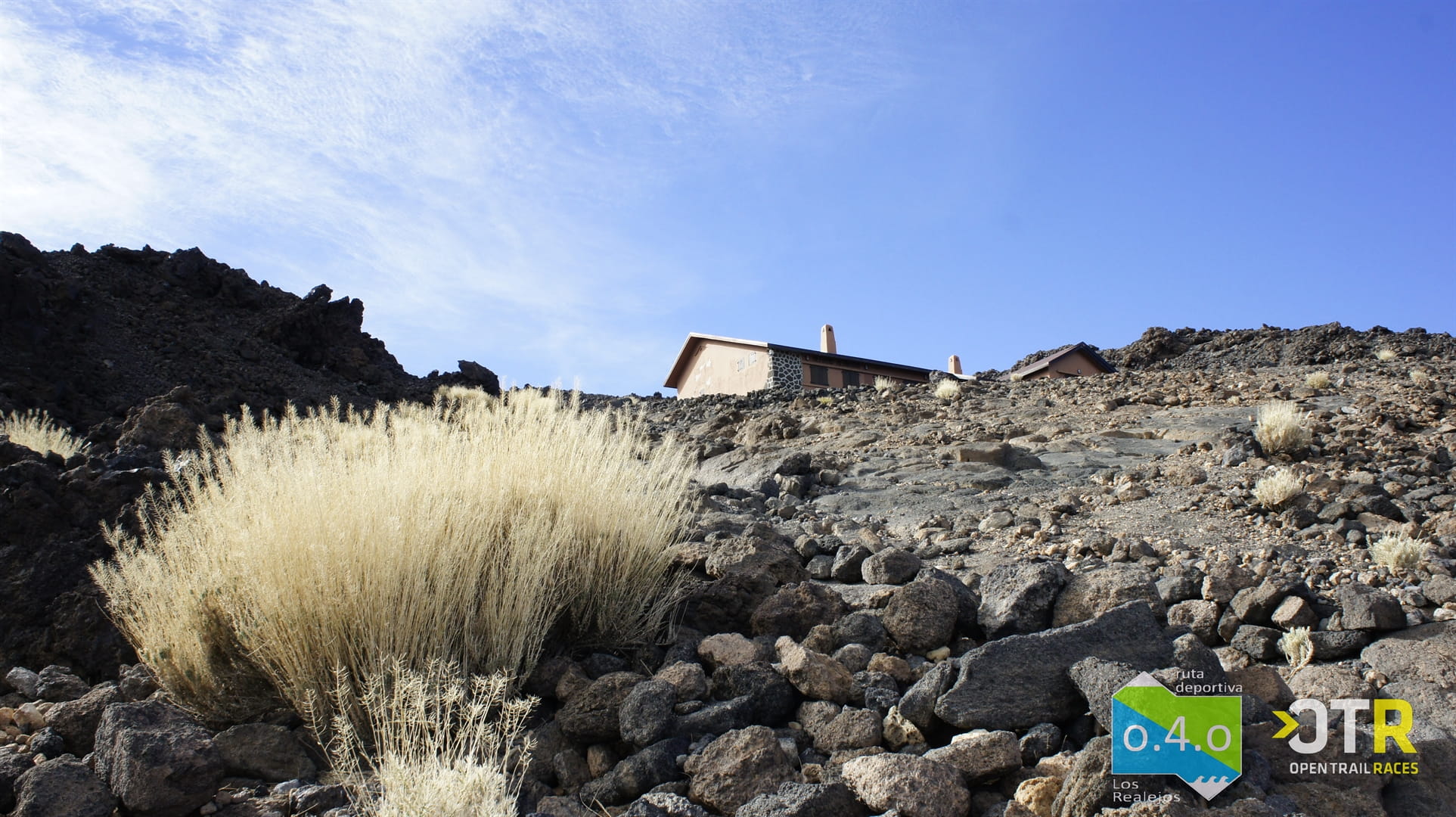 Paysage rocheux avec des bâtiments sur El Teide, Tenerife, ciel dégagé, logo OTR visible.
