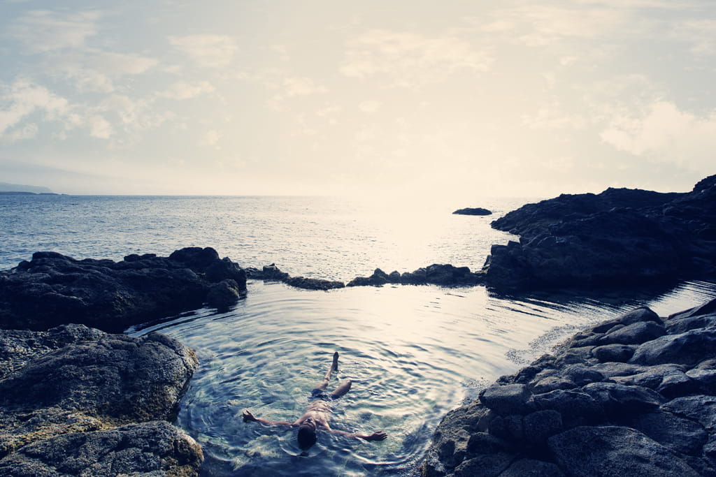Personne flottant dans une piscine naturelle entourée de rochers au bord de l’océan à Tenerife.