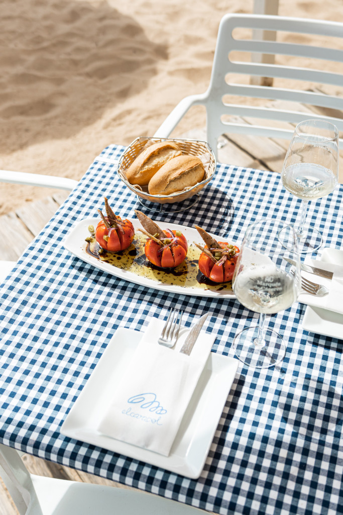 Table avec tomates farcies, pain et verre de vin devant la plage d’El Ancla à Tenerife.
