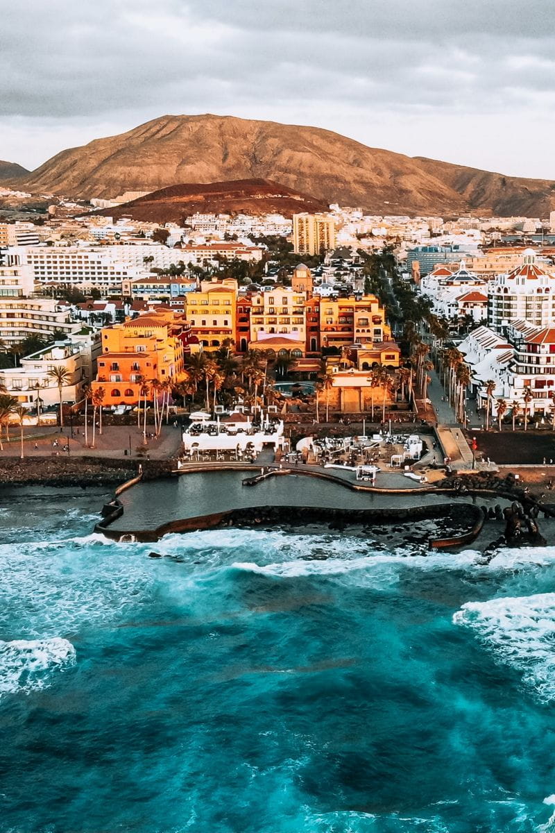 Vue aérienne de la côte de Tenerife avec des bâtiments et une montagne en arrière-plan.