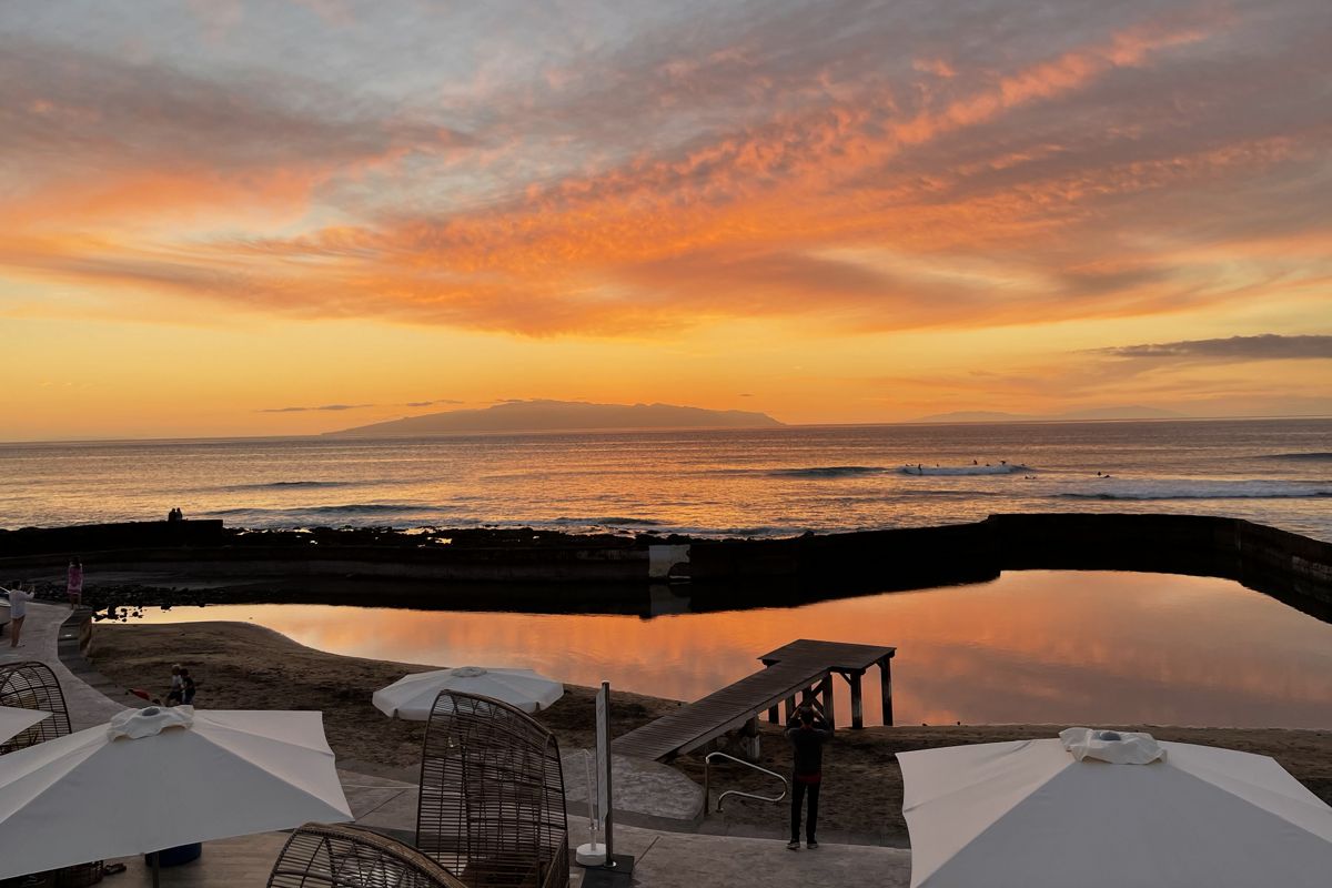 Coucher de soleil sur l’océan à Tenerife, avec un ciel orange et des parapluies au premier plan.