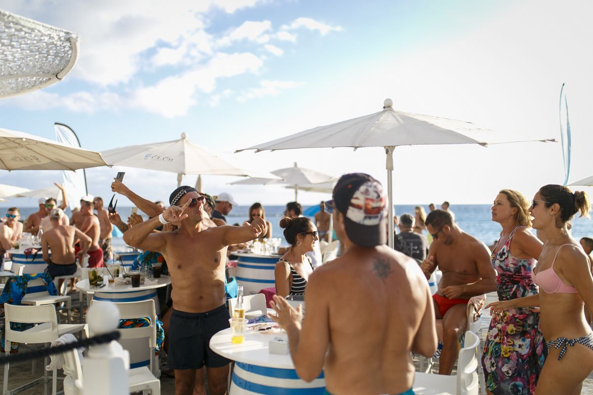 Des gens profitant d’une fête à la plage à Tenerife, avec parasols et tables.