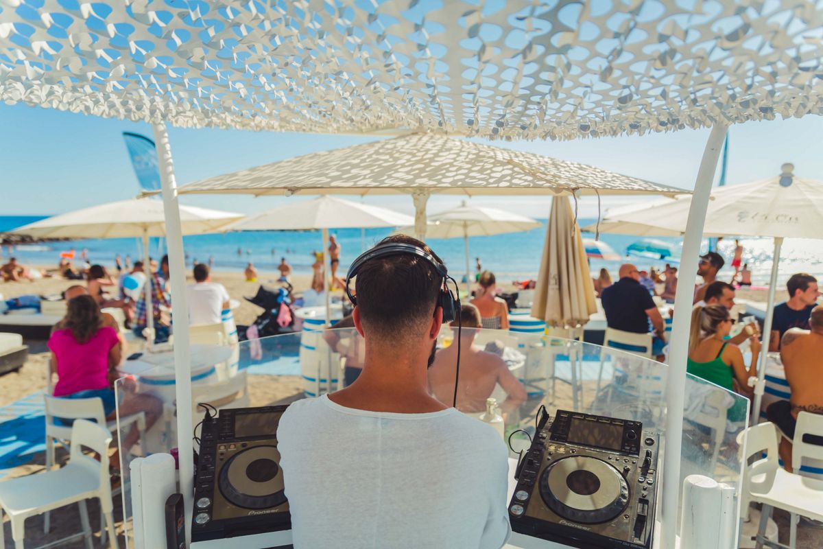 DJ jouant de la musique sur une plage à Tenerife avec des gens profitant de la mer.
