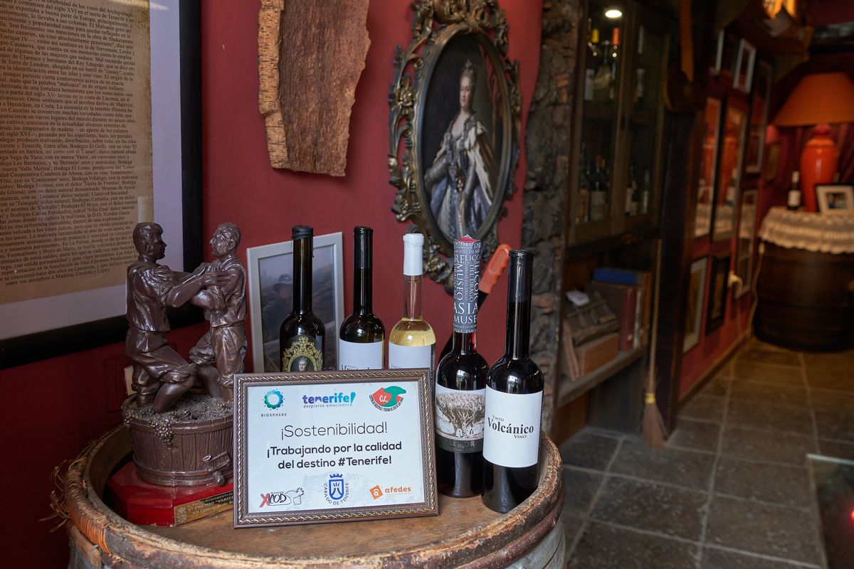 Des bouteilles de vin et des enseignes de durabilité sur un tonneau dans un établissement de Tenerife.