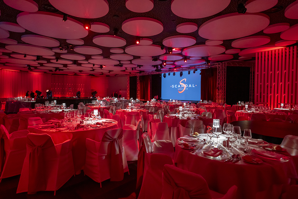 Salle d’événement avec tables décorées et écran arborant le logo SCANDAL Show Tenerife.