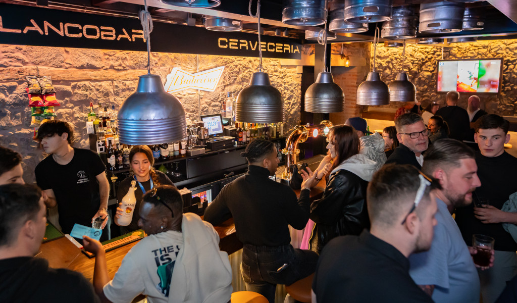 Des gens discutant au bar d’une brasserie à Tenerife, avec une enseigne Budweiser.