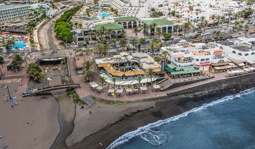 Vue aérienne sur la plage et la zone urbaine de Tenerife avec des bâtiments et des restaurants à proximité.