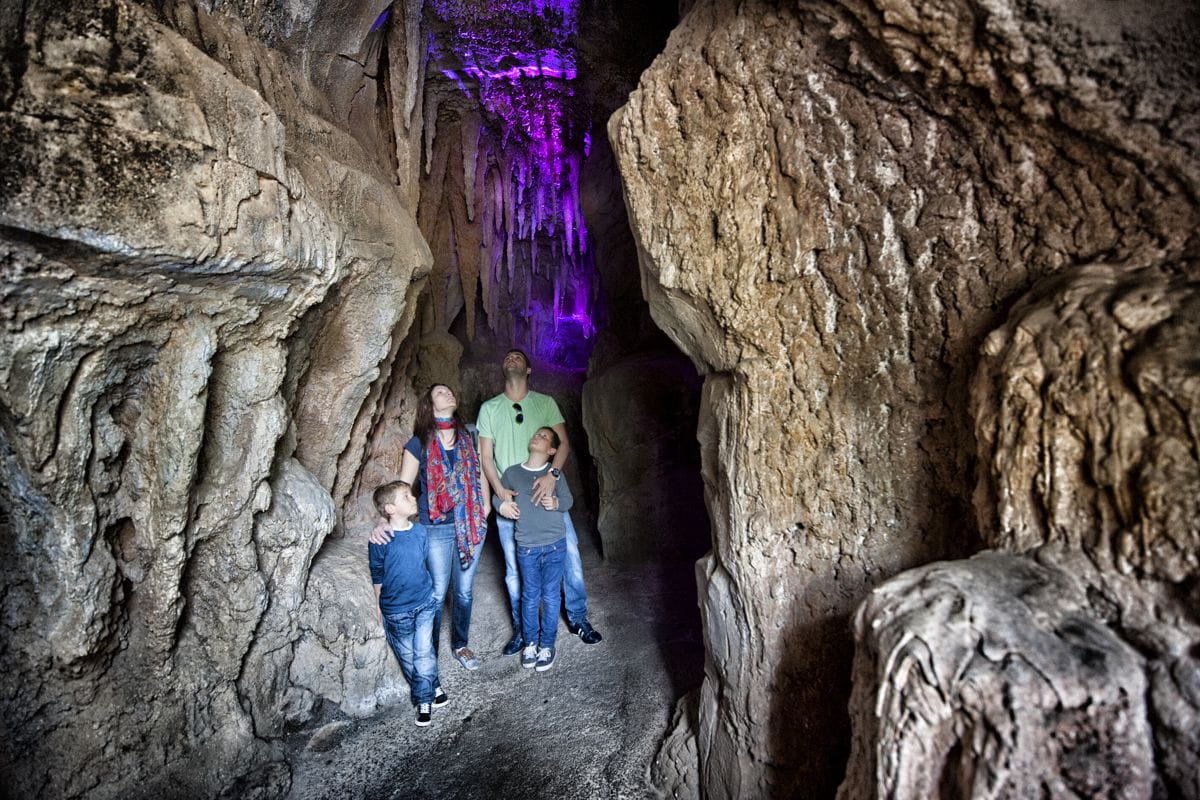 Famille explorant une grotte à Tenerife, avec une lumière violette mettant en valeur l’intérieur.