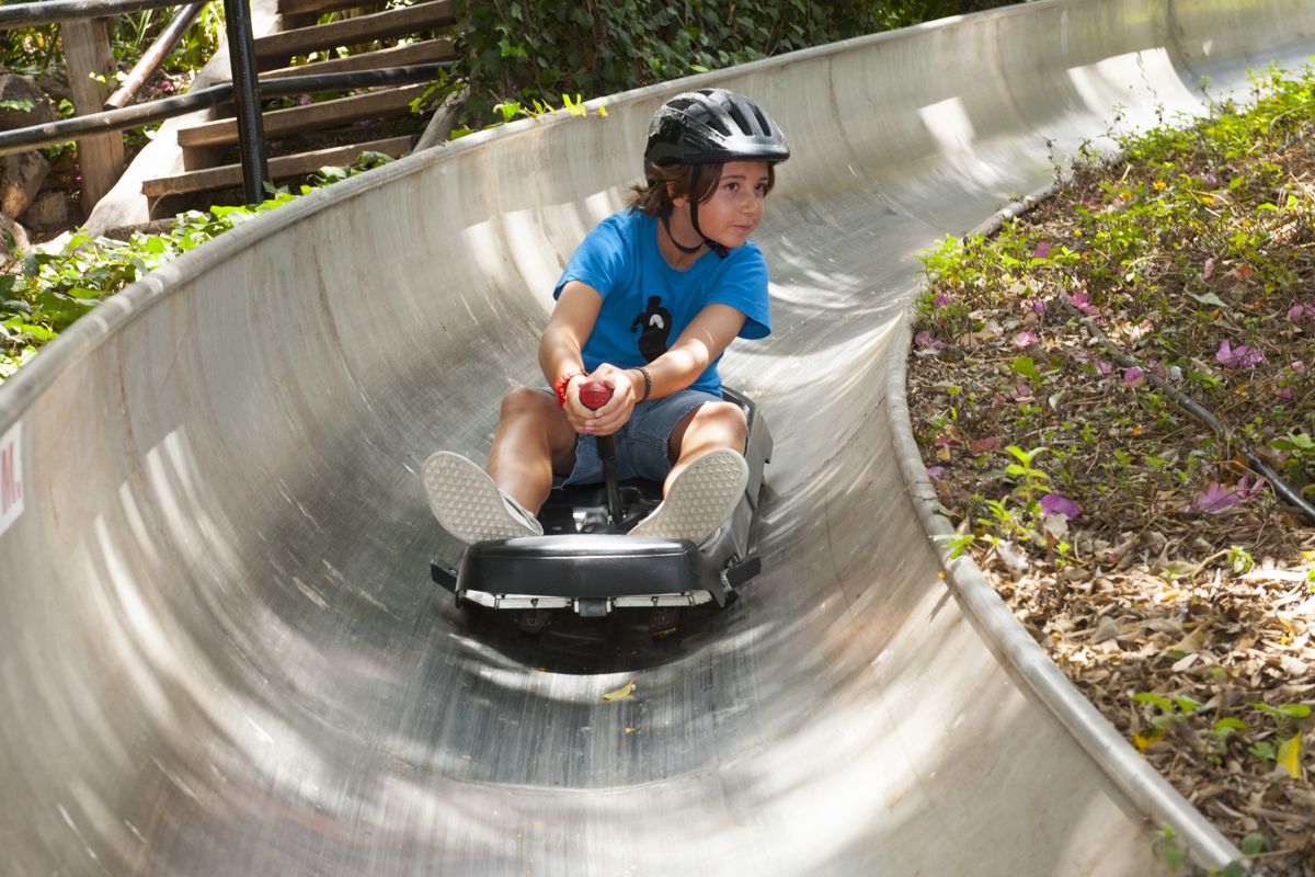 Garçon avec un casque noir glissant sur un toboggan métallique courbé à Tenerife.
