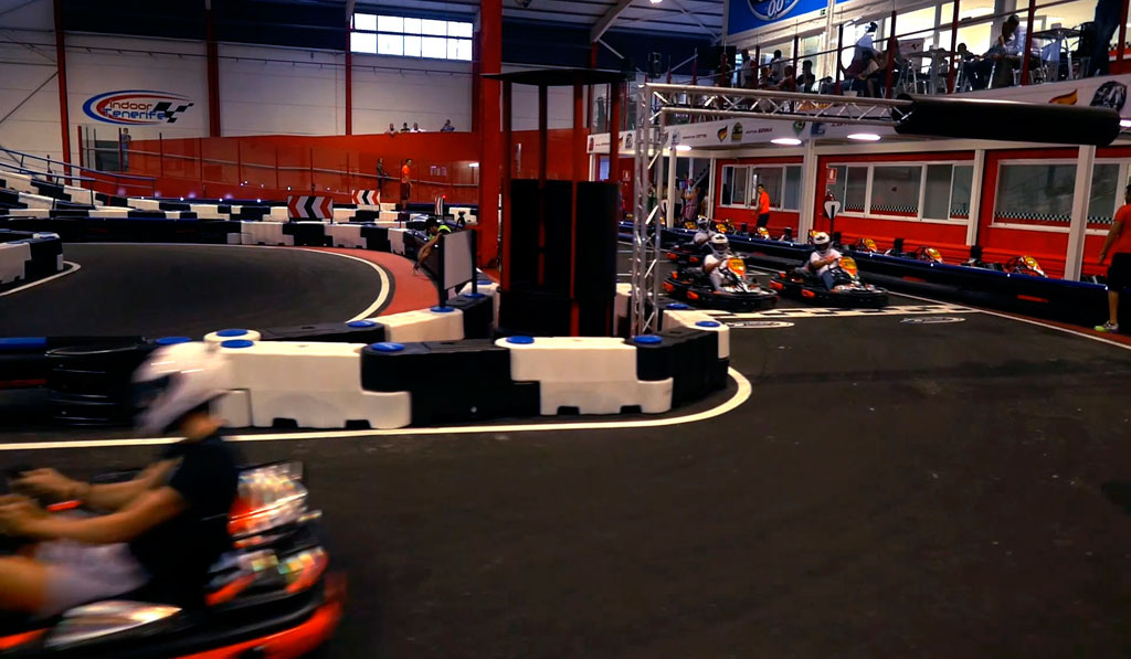 Des karts en course sur le circuit intérieur de Tenerife avec des spectateurs en arrière-plan.