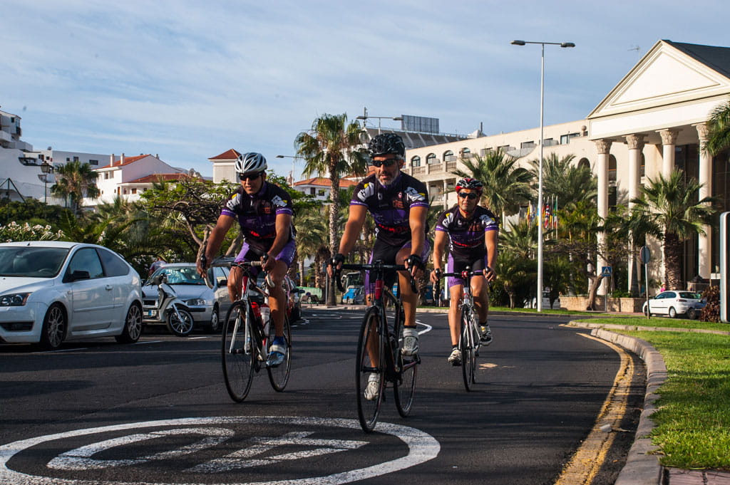 Cyclistes à San Miguel de Abona, Tenerife, dans une rue avec des bâtiments et des palmiers.