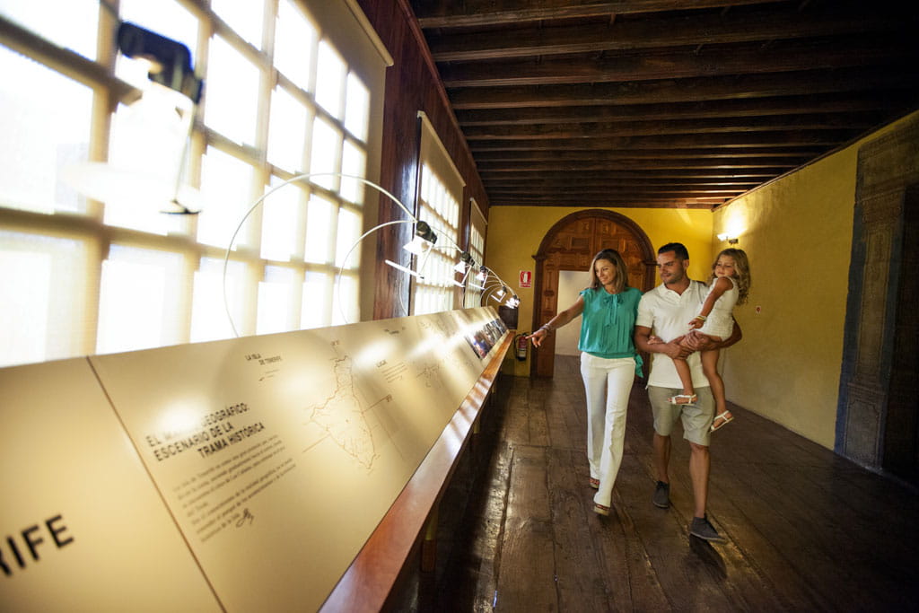 Famille visitant un musée à Tenerife, observant une exposition éclairée dans un couloir en bois.