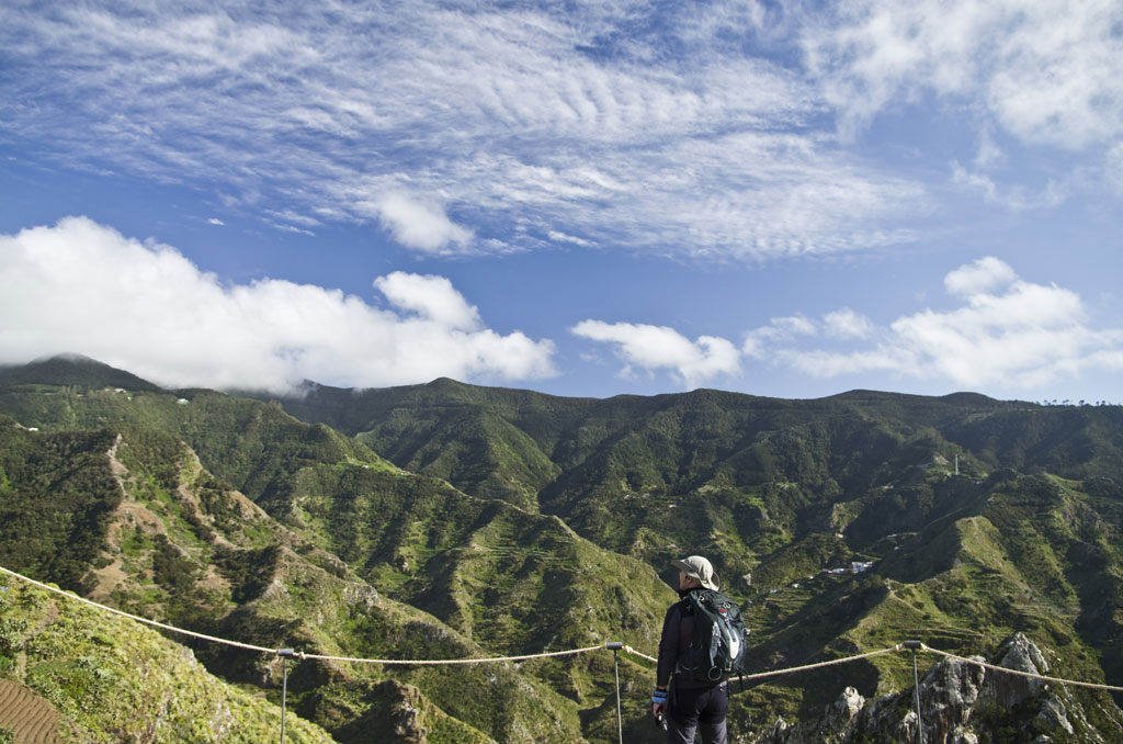 Personne observant les montagnes verdoyantes d’Anaga à Tenerife sous un ciel partiellement nuageux.